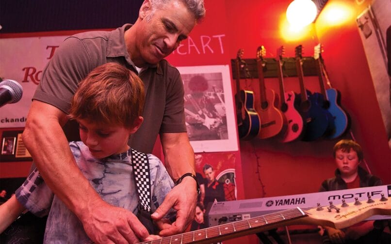 A teacher instructs a student on the proper way to hold a guitar.